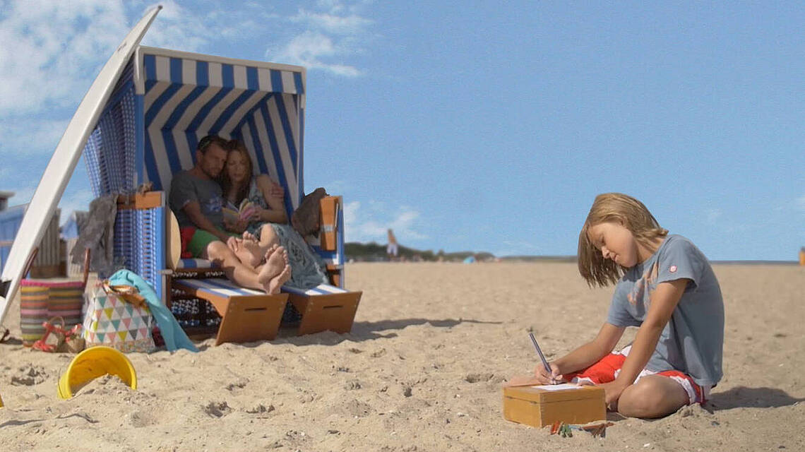 Ein Kind buddelt im Sand vor einem Strandkorb