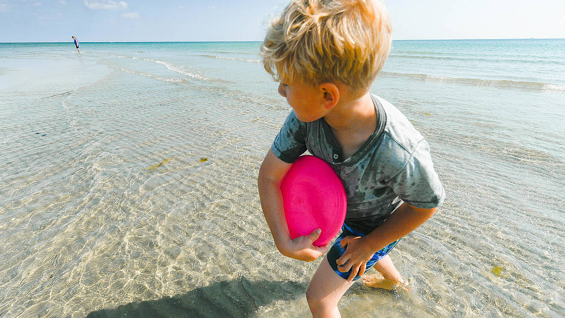 Ein kleiner Junge wirft eine Frisbee am Strand