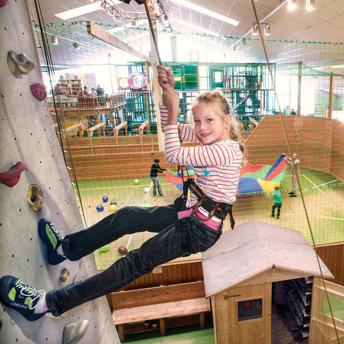 Funhalla Indoor Klettern Ein junges Mädchen hängt an der Kletterwand an einem Seil