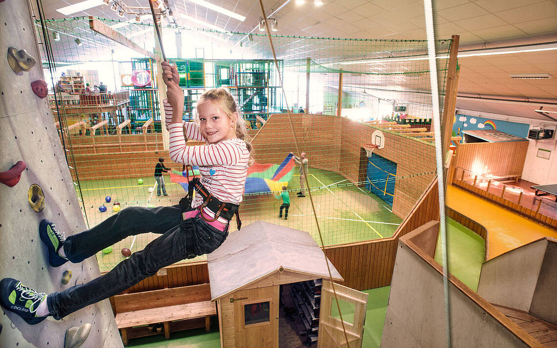 Funhalla Indoor Klettern Ein junges Mädchen hängt an der Kletterwand an einem Seil