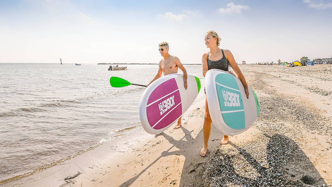 Ein Pärchen trägt SupBoards am Strand