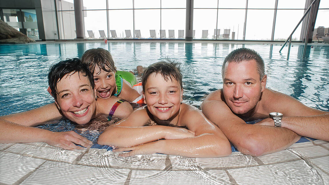 Eine Familie sitzt am Poolrand und schaut in die Kamera