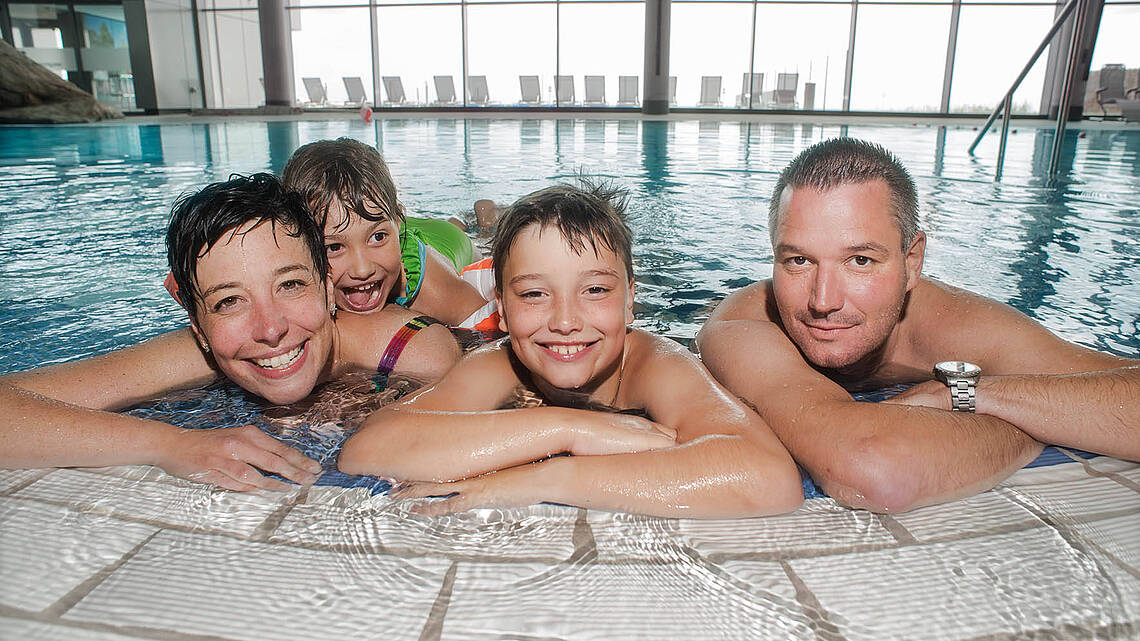Eine Familie sitzt am Poolrand und schaut in die Kamera