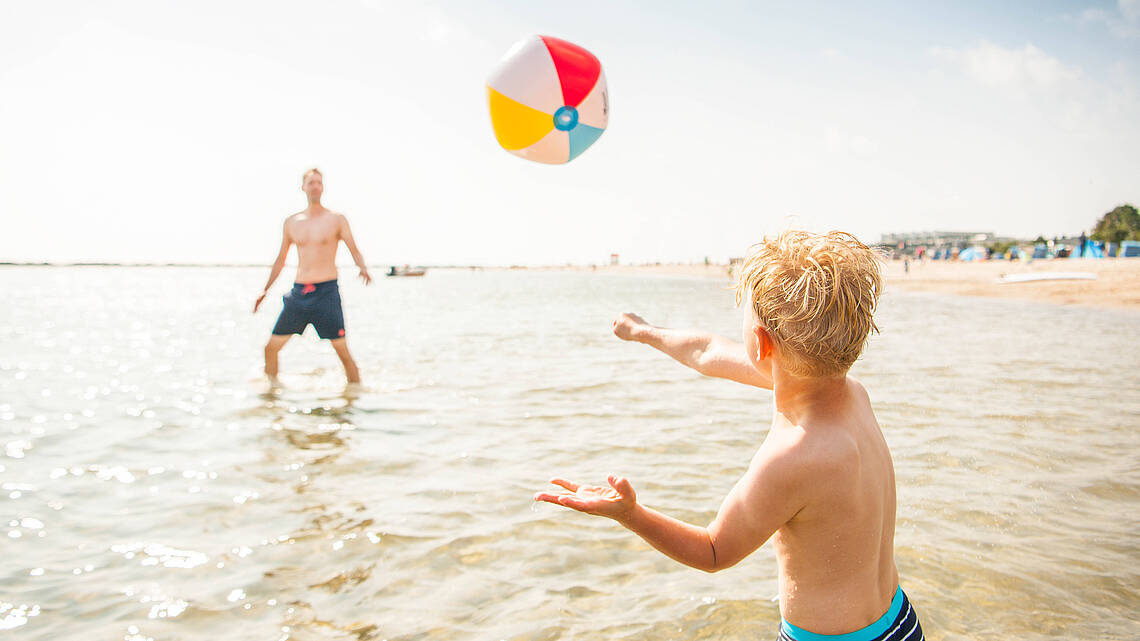 Vater und Sohn spielen Wasserball im flachen Wasser