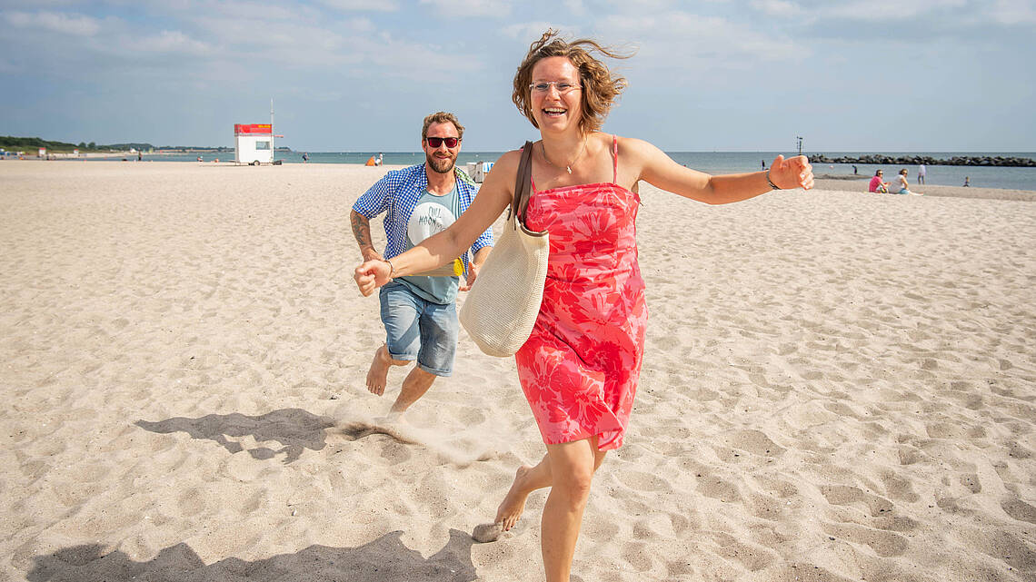 Ein fröhliches Paar rennt am Strand entlang