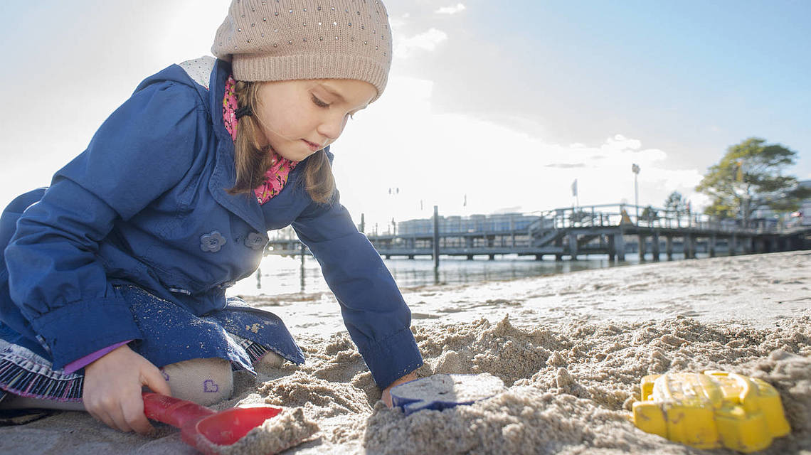 Ein kleines Mädchen baut eine Sandburg am Strand