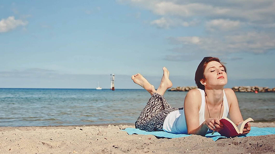 Eine Frau liest entspannt ein Buch am Strand